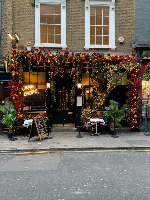 The exterior of a florist shop adorned with a vibrant, dense garland of red, orange, and yellow flowers, including roses and chrysanthemums, intertwined with greenery. The storefront features large wi